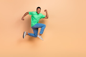 Full size photo of optimistic active guy dressed green t-shirt denim pants fast running in empty space isolated on beige color background