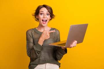 Photo portrait of attractive young woman shocked point netbook dressed stylish knitted khaki clothes isolated on yellow color background - obrazy, fototapety, plakaty