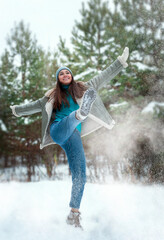 Beautiful young woman in winter clothes jumping and having fun in the snow
