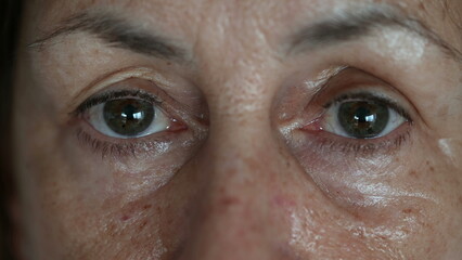 Tight macro close-up of elderly woman gazing at camera. Face and eyes of senior caucasian person