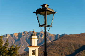 Church Tower of Saints Fedele and Simone and Street Lamp with Mountain in a Sunny Day in Vico Morcote, Ticino in Switzerland.