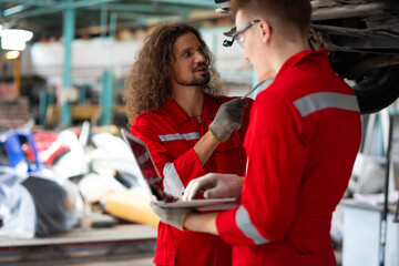 car lift under vehicle. Caucasian manager use laptop computer and hispanic latin male mechanic repairs car in garage. Car repair maintenance and auto service garage concept