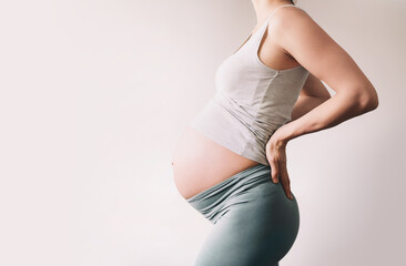 Beautiful young pregnant woman in good fit holds hands on her belly. Happy mother waiting for baby...