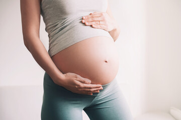 Beautiful young pregnant woman in good fit holds hands on her belly. Happy mother waiting for baby birth during pregnancy.