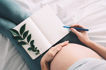 Pregnant woman with beautiful belly makes notes or check list in paper diary. Concepts of...