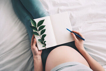 Pregnant woman with beautiful belly makes notes or check list in paper diary. Concepts of preparation for baby birth, tips for a healthy pregnancy. - obrazy, fototapety, plakaty