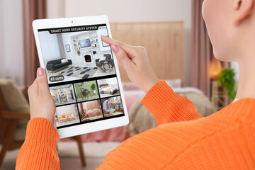 Woman using smart home security system on tablet computer indoors, closeup. Device showing...