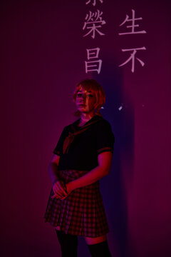 anime woman in wig and school uniform in neon light on purple backdrop with hieroglyphs projection