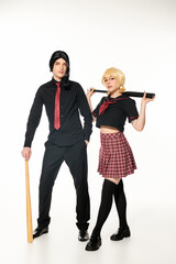 full length of young cosplayers in dark school uniform and wigs with baseball bats on white