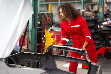 Hipster hispanic male car repair worker taking off car bumper part to get it repaired. male...