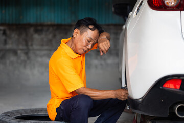 Hot and tired. repairing car wheel and disk brake and  replace tires on wheels. Senior Asian thai...