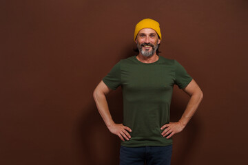 Happy confident middle-aged man standing with hands on sides on brown background. Posture and joyful smile convey sense of confidence, contentment, and success. mature individual in assertive stance.