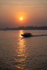 Naklejka premium Beautiful golden hour sunset at Amazon Tapajos river with a speed boat and agricultural silos to store soybeans. Concept of environment, ecology, conservation, nature, climate change, global warming.