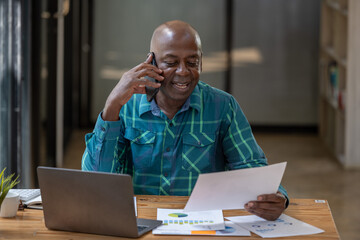 Black senior man working happily with document report. Using the phone talking with team.