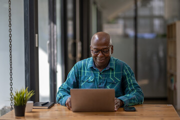 Senior black man in casual clothes happily uses laptop to work When he reached retirement age, he...