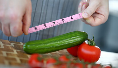 Male Hands Measure Green Ripe Cucumber Length. Chef with Pink Centimeter Meter Vegetable at Kitchen. Organic Red Tomato. Man Showing Measurement of Fresh Ingredient. Partial View Photography