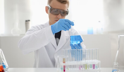 Fototapeta premium A male chemist holds test tube of glass in his hand overflows a liquid solution of potassium permanganate. Conducts an analysis reaction takes various versions of reagents using chemical manufacturing