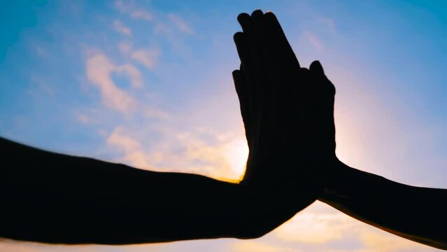 Woman and man silhouettes are giving a high fives hand gesture against the sunset or sunrise sky - sun lens flare, close up view. Cheerful, friendship, greeting and positive concept