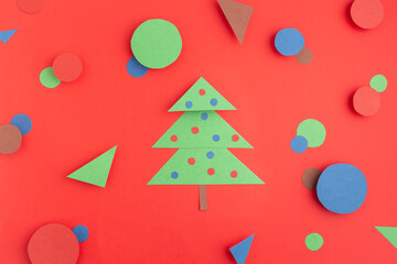 green paper Christmas tree on red, blue and brown circles and triangles concept creative idea flat lay color contrast