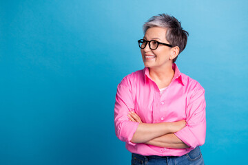 Photo of funny pleasant woman dressed pink shirt in glasses arms folded look at sale empty space isolated on blue color background