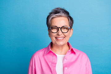 Photo of good mood optimistic woman with short hairstyle dressed pink shirt in glasses smilimg at camera isolated on blue color background - obrazy, fototapety, plakaty