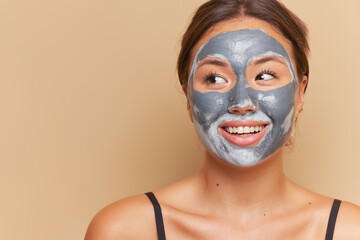 Close-up portrait of cute girl smiling over backdrop, doing cosmetic procedures with clay facial mask, skincare product concept, copy space