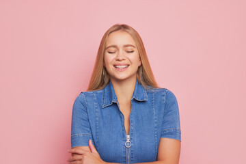 Fototapeta premium Blonde young woman with long hair in glasses dressed in denim shirt posing isolated on pink background, happy life concept, copy space