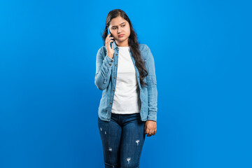 Portrait of an unhappy Indian women speaking over the smart phone, isolated on blue background