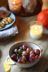 Cup of tea or coffee, plate with desserts, dried oranges, bowl of grapes, scented candles, vintage books, pumpkins and autumn leaves on the table. Autumnal hygge. Selective focus.