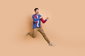 Fototapeta na wymiar Full body photo of jumping crazy promoter directing fingers empty space mega sale proposition zara store isolated on beige color background