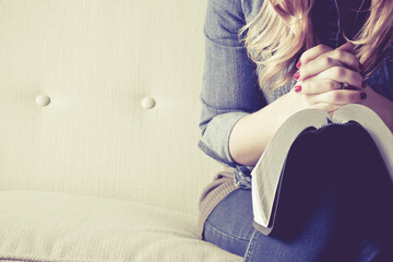 Woman's hands in prayer held over a Bible on a couch. 