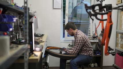 Male bicycle mechanic working in workshop. Bike repairman changing tire on racing road bike in repair shop. Cycle technician fitting new tire and tube to wheel of road bike. Workstation. 