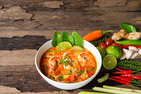 Tom Yum Goong or Shrimp soup spicy sour Soup Traditional food in Thailand contains chili, lime,lemongrass, lime leaf, along with cooked rice in a white dish on the old wood background from top view.