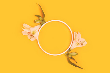 Round frame made of green leaves and white alstroemeria flowers on a yellow background.