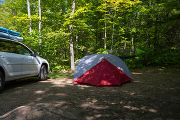 Set up campsite in the forest - tent with hanging hammock and parked SUV truck with inflated paddle boards on the roof in the background. Summer vacation, adventure, road trip concept. - Powered by Adobe