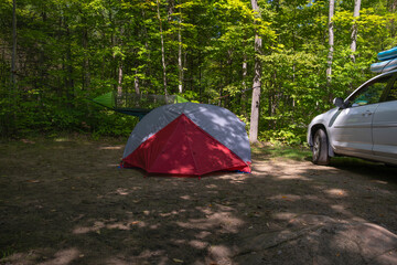 Set up campsite in the forest - tent with hanging hammock and parked SUV truck with inflated paddle boards on the roof in the background. Summer vacation, adventure, road trip concept.