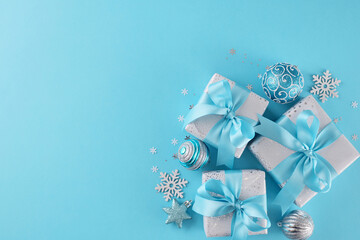 Discover the perfect presents and immerse yourself in the holiday spirit. Top view photo of beautiful gift boxes, holiday baubles, snowflakes, stars on blue background with advertising zone