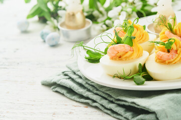 Stuffed or deviled eggs yolk, shrimp, pea microgreens with paprika for easter table decorate fresh cherry or apple blossoms on white light background. Happy Easter traditional dish concept. Mock up.