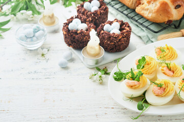 Stuffed or deviled eggs yolk, shrimp, pea microgreens with paprika for easter table decorate fresh cherry or apple blossoms on white light background. Happy Easter traditional dish concept. Mock up.