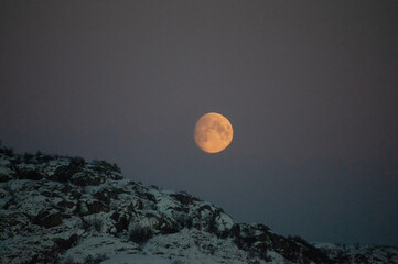 Naklejka na ściany i meble A near full moon is slowly creeping behind a mountain along the norwegian coast on an early winter morning near the town of Bodo.