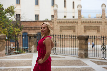 Beautiful blonde mature woman dressed in an elegant dress parading down the street like a model. The woman is happy and enjoying the day.