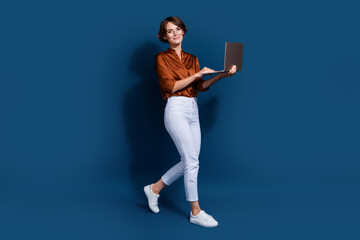 Fototapeta na wymiar Full length photo of positive sweet lady wear brown shirt walking working modern gadget isolated blue color background