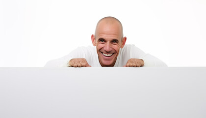 A playful bald man peeking over a white wall with a smile on his face