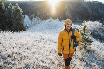 A guy walks smiling against the background of mountains, the glare of sunlight illuminates a man in the mountains, a happy tourist trekking in a mountainous area.