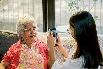 The grandmother poses very happily in front of a smartphone camera while her granddaughter takes...