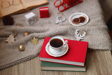 Bowl of cookies, cup of tea, dry oranges, pine cones, books, reading glasses, small presents, various Christmas decorations and lit candles on the table. Cozy Christmas hygge. Selective focus.
