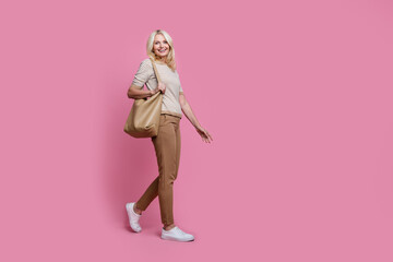 Fototapeta na wymiar Full size profile portrait of gorgeous satisfied person hold bag walking empty space isolated on pink color background