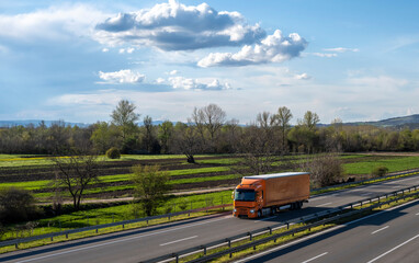 Fototapeta na wymiar Orange semi trailer truck driving on a highway with dramatic sky in the background. Transportation vehicle. Orange truck driving on asphalt road in a rural landscape.