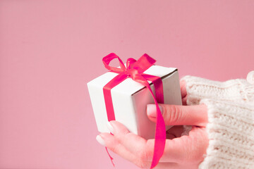 white gift box with pink ribbon bow in woman hand with white sweater with copy space.