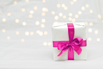 Decorative white gift box with a large pink bow against a background bokeh of lights